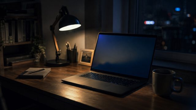 夜のデスクでほのかに光るノートパソコンとマグカップ